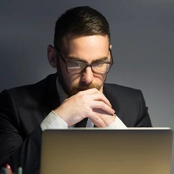 A bearded person wearing a formal suit looking at his laptop