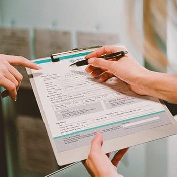 Someone filling a form while another person points at the form